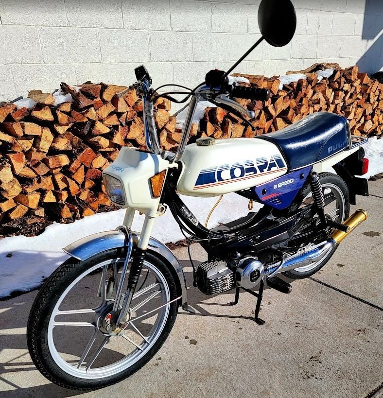 A white Puch Cobra with the blue and red decal and mag wheels
